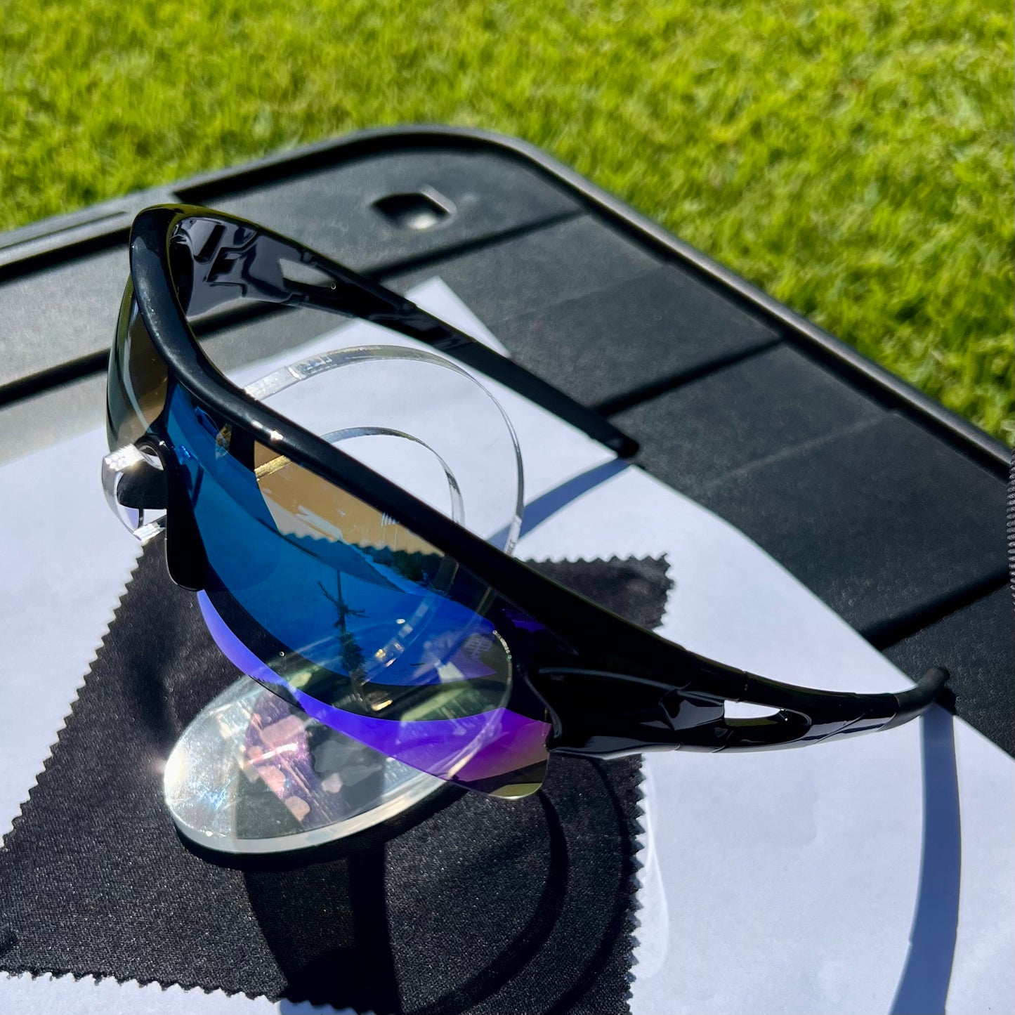 A pair of Sportiq OptiView - Sky Blue professional sport sunglasses with blue reflective lenses and black frame, polarized UV400, polycarbonate frame with TAC lens, displayed on a grass background.