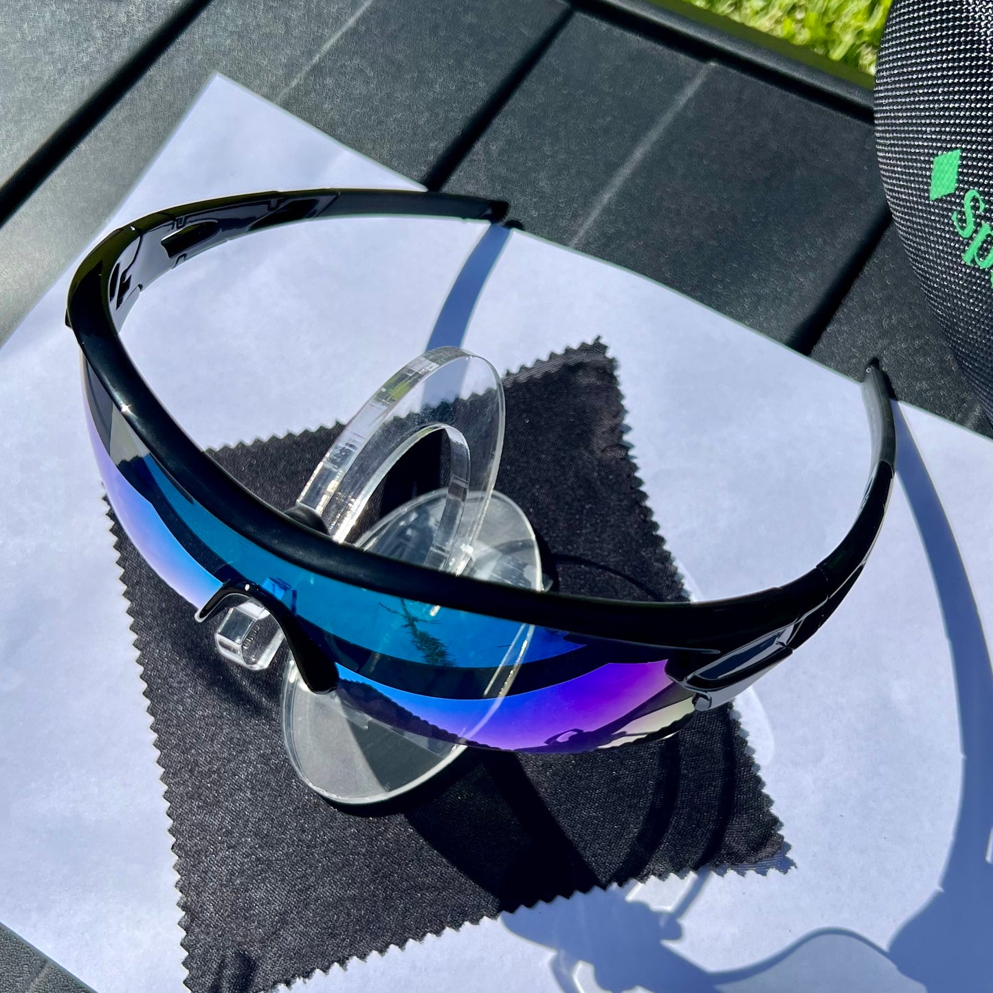 A pair of Sportiq OptiView - Sky Blue professional sport sunglasses with blue reflective lenses and black frame, polarized UV400, polycarbonate frame with TAC lens, displayed on a grass background.