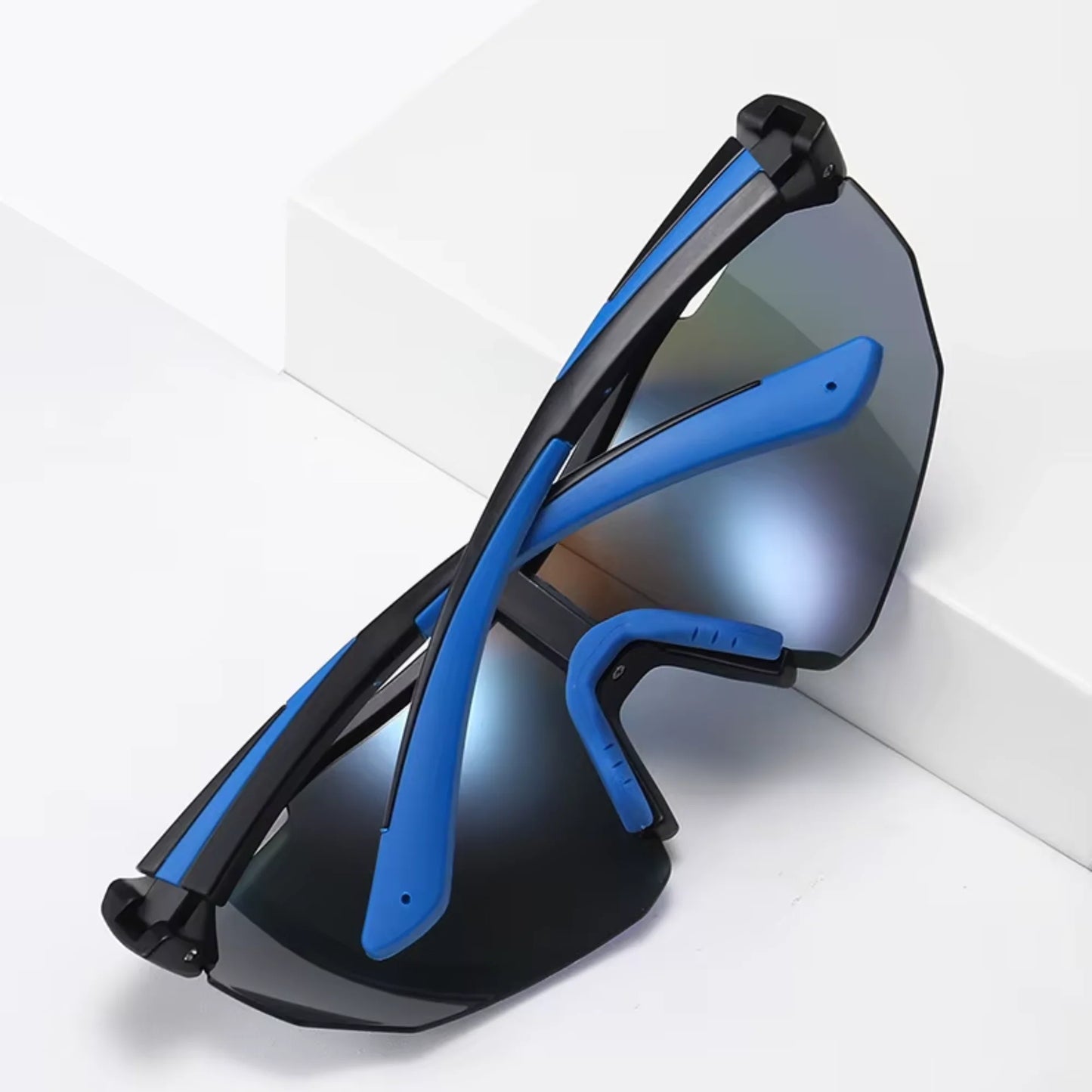 A pair of Sportiq ClarityX - Azure professional sport sunglasses with blue reflective lenses and black frame, polarized UV400, polycarbonate frame with TAC lens, displayed on a grass background.