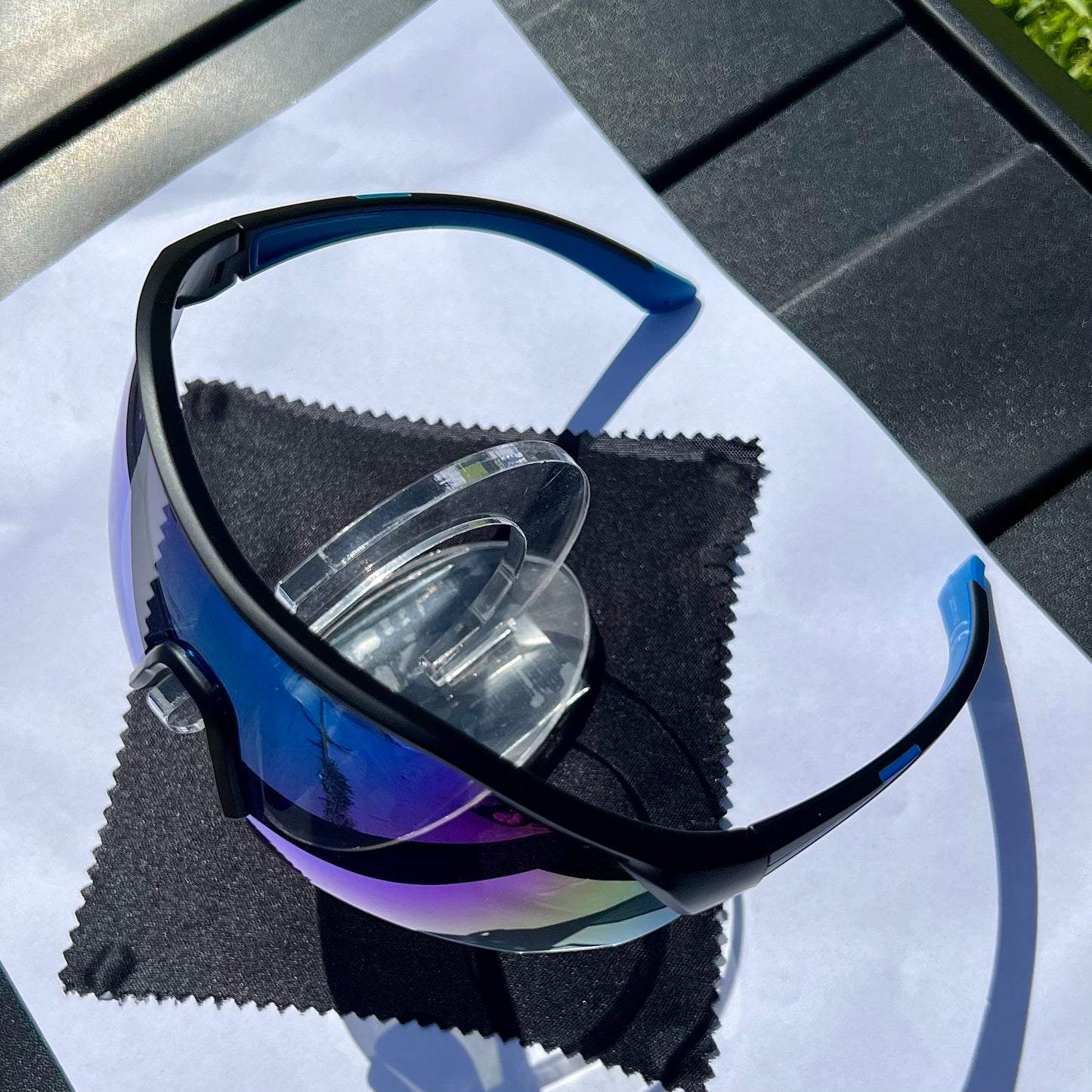 A pair of Sportiq ClarityX - Azure professional sport sunglasses with blue reflective lenses and black frame, polarized UV400, polycarbonate frame with TAC lens, displayed on a grass background.
