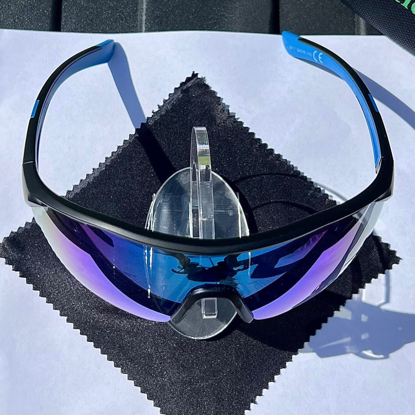 A pair of Sportiq ClarityX - Azure professional sport sunglasses with blue reflective lenses and black frame, polarized UV400, polycarbonate frame with TAC lens, displayed on a grass background.