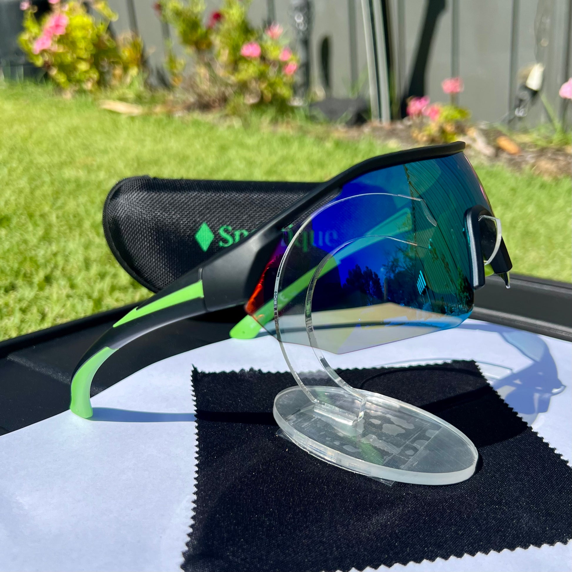 A pair of Sportiq ClarityX - Emerald professional sport sunglasses with green reflective lenses and black frame, polarized UV400, polycarbonate frame with TAC lens, displayed on a grass background.