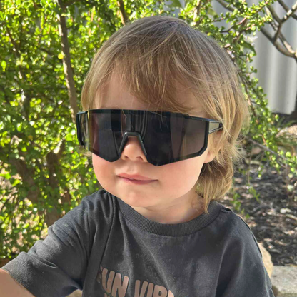 A child wearing a pair of Sportiq JNR kids Jet Black sport sunglasses with black lenses and black frame, UV400, polycarbonate frame with polycarbonate lens.
