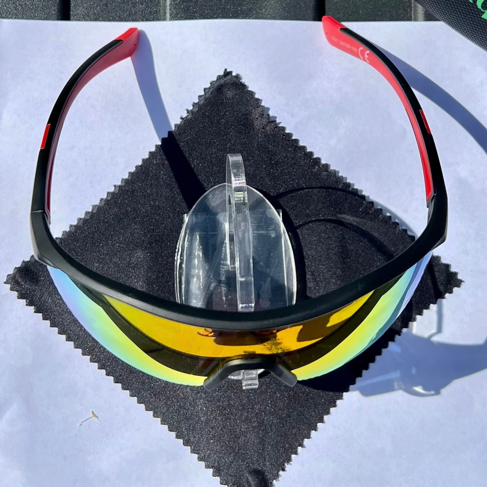 A pair of Sportiq ClarityX - Ruby professional sport sunglasses with red reflective lenses and black frame, polarized UV400, polycarbonate frame with TAC lens, displayed on a grass background.